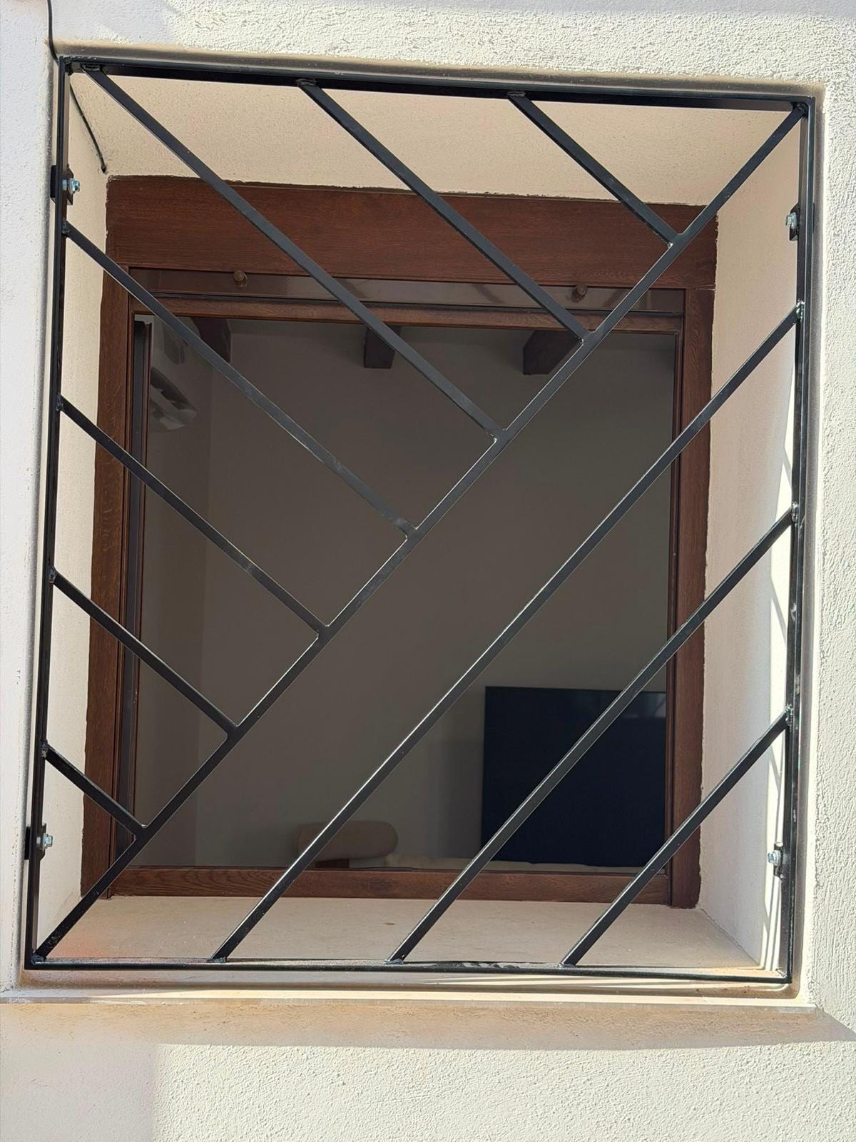 reja diagonal negra instalada en una ventana con carpintería de madera