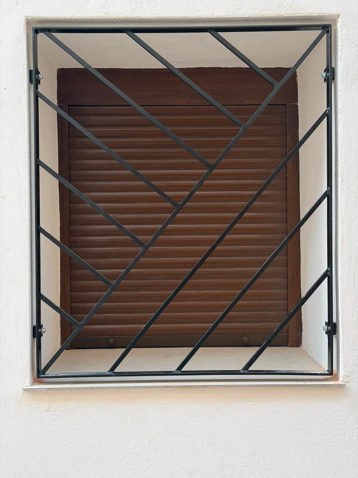 reja diagonal negra instalada, vista frontal centrada sobre persiana marrón