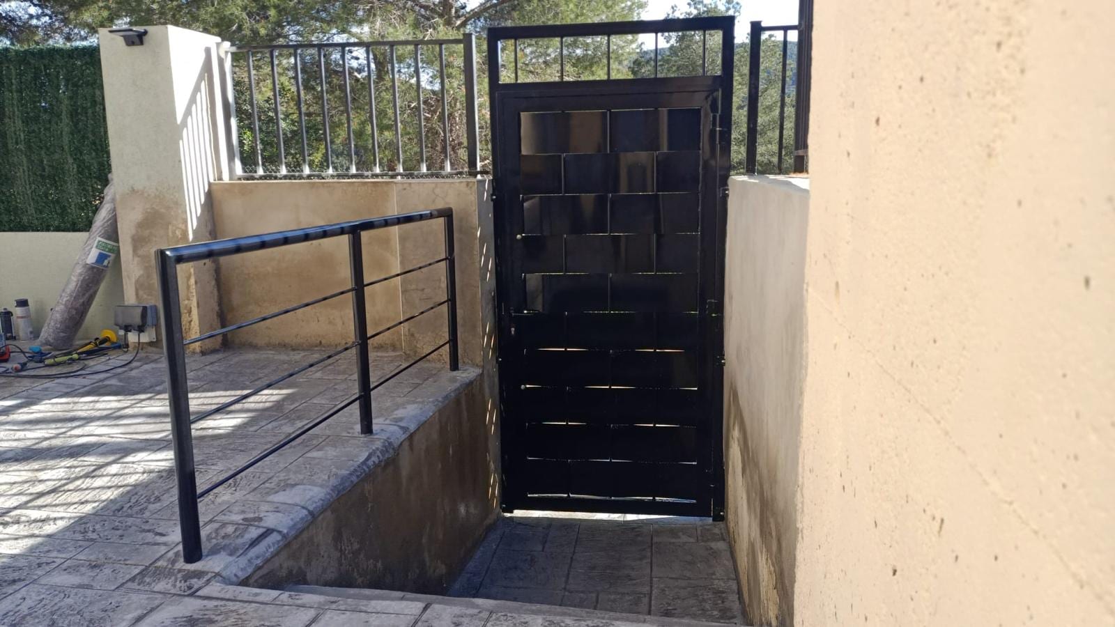 puerta peatonal de chapas entrelazadas y barandilla negra en acceso a vivienda